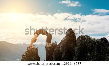 man doing complex Yoga exercise headstand. Amazing Yoga landscape in beautiful mountains. Dangerous stunts traceur standing on his hands on the edge of a cliff.