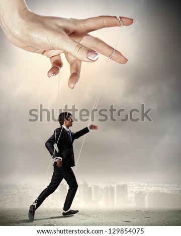Businessman marionette on ropes controlled by puppeteer against city background