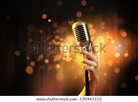 Female Hand Holding A Single Retro Microphone Against Colourful Background