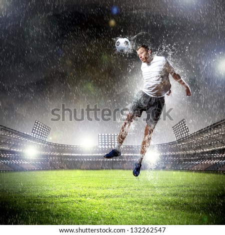 football player in white shirt striking the ball with head at the stadium under the rain