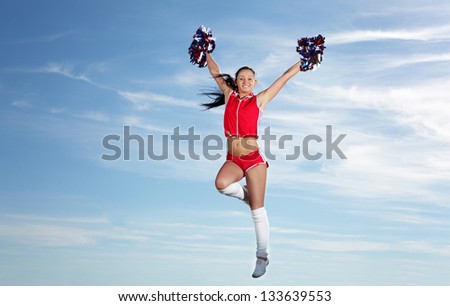 Young beautiful female cheerleader in uniform jumping high