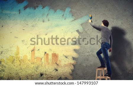 Young man painting a yellow colour cityscape on the wall