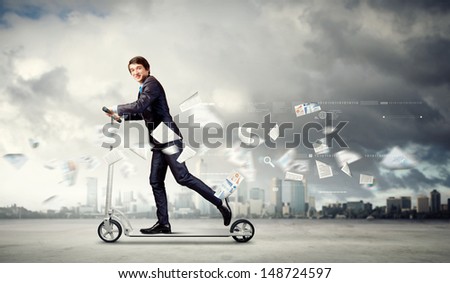 Image of young businessman in black suit riding scooter