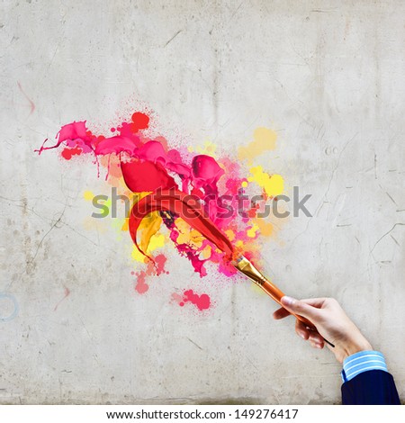 Close-up of human hand holding paint brush making colorful paint splashes