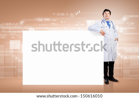 Young male doctor leaning upon blank banner. Place for text
