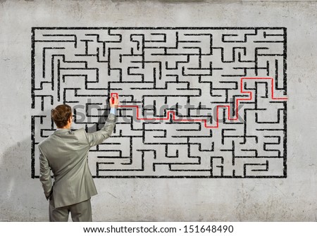 Back view image of young businessman trying to find way out of maze