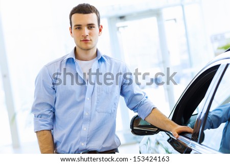 Handsome young man consultant at car salon standing near car