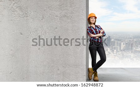 Image of young woman builder wearing helmet and leaning on blank wall