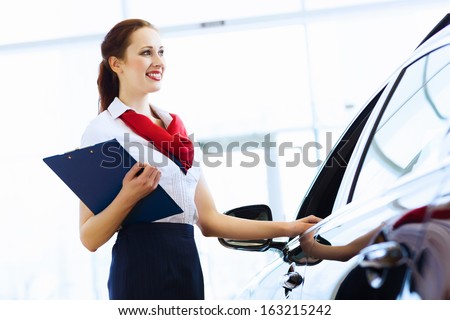 Young attractive woman consultant of car center standing near car