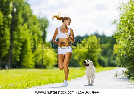 Young attractive sport girl running with dog in park