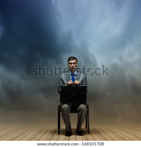 Young businessman sitting on chair with suitcase on knees