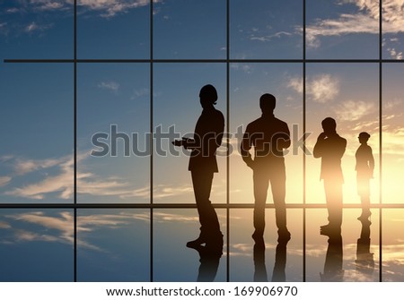 Silhouettes of businesspeople standing against panoramic office window