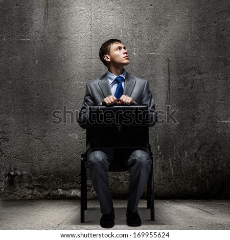 Young businessman sitting on chair with suitcase on knees
