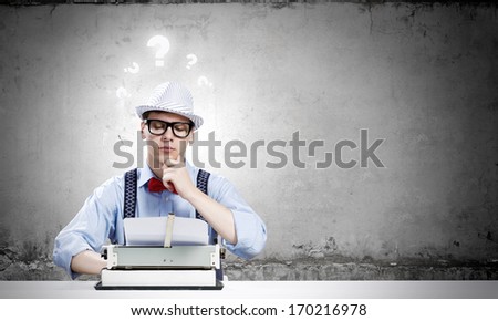 Young funny man in glasses writing on typewriter