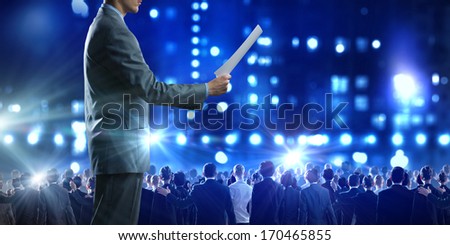 Back view of businessman speaker standing on podium in lights