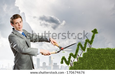 Young businessman cutting bush in shape of graph