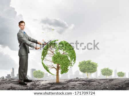 Young businessman cutting tree with scissors in shape of Earth planet