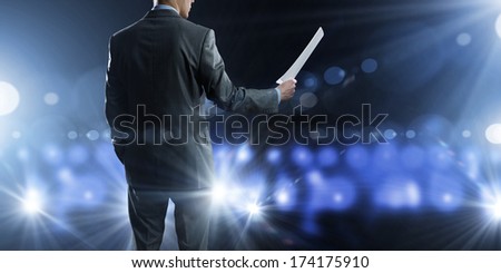 Back view of businessman speaker standing on podium in lights