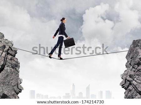 Young confident businesswoman walking on rope above gap
