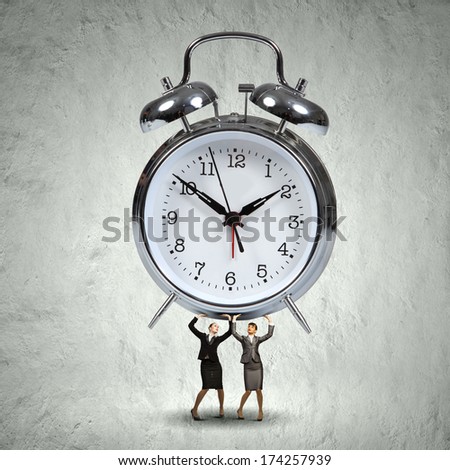 Two businesswoman lifting huge alarm clock above head