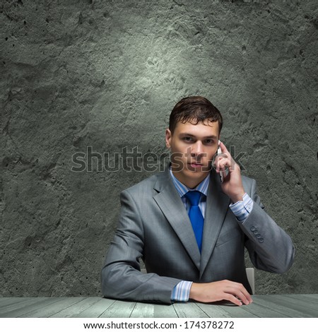 Businessman sitting under rain talking on mobile phone