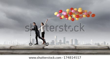 Young businessman and businesswoman riding scooter on roof of building