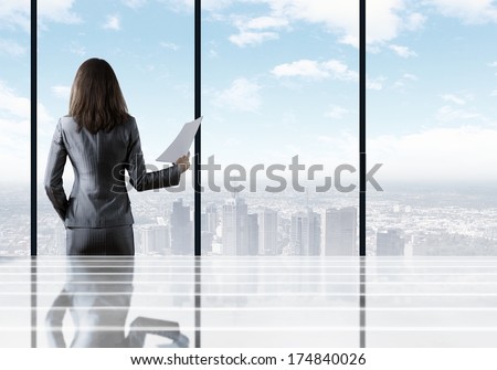 Businesswoman Standing With Back Against Office Window Holding Documents In Hand