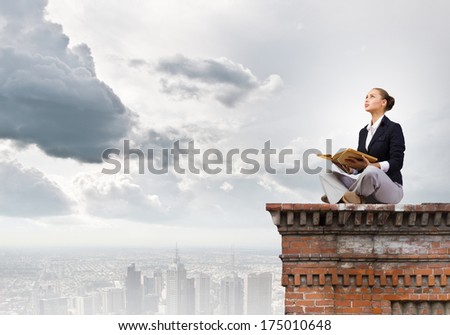 Young attractive woman sitting on top of building and reading book
