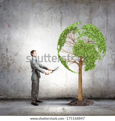 Young businessman cutting tree with scissors in shape of Earth planet
