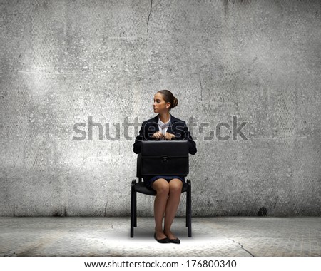 Young upset businesswoman with suitcase sitting on chair