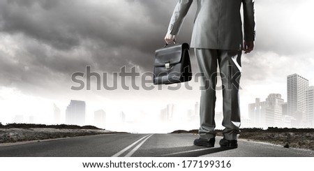 Back view of businessman on road with suitcase in hand