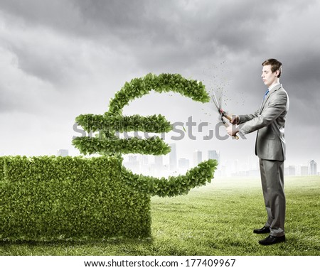 Young businessman cutting bush in shape of euro symbol