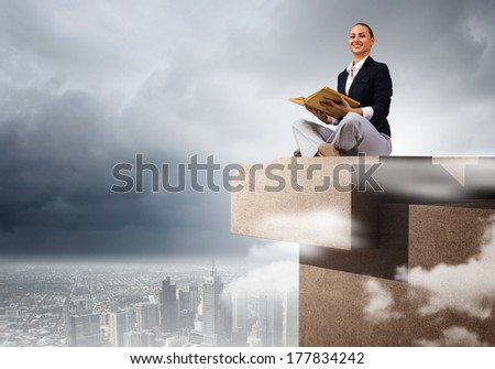 Young attractive businesswoman sitting on roof of building and reading book