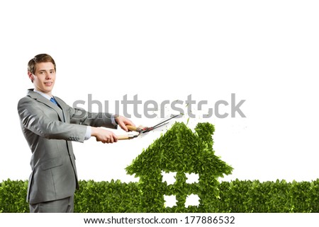 Young businessman cutting green bush in shape of house
