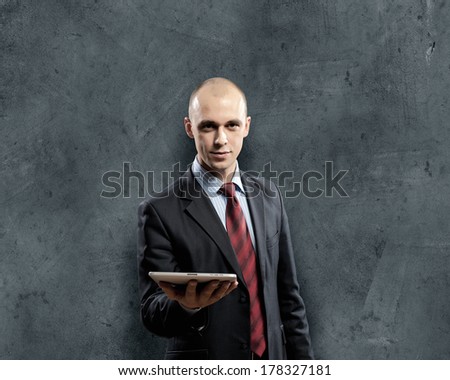 Young businessman against grey background holding tablet pc
