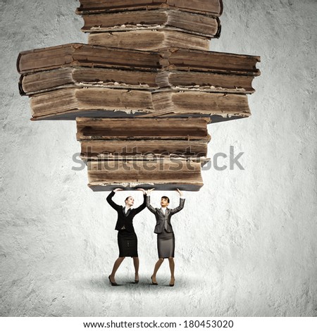 Two young ladies lifting pile of old books above head