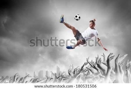 Football player in jump kicking the ball supported by fans