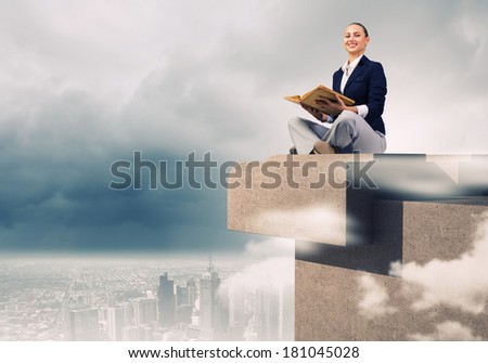 Young attractive businesswoman sitting on roof of building and reading book