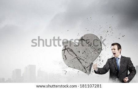 Young businessman breaking stone heart with punch