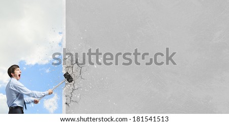 Young determined businessman breaking wall with hammer