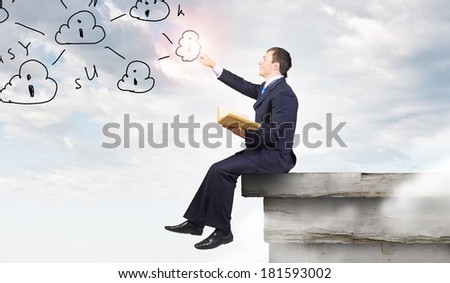 Young businessman reading book sitting on roof of building
