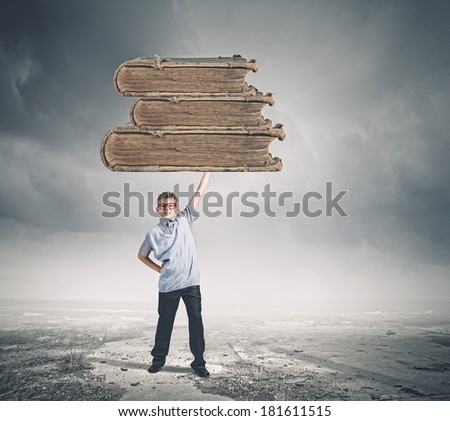 Boy of school age in glasses lifting a pile of books