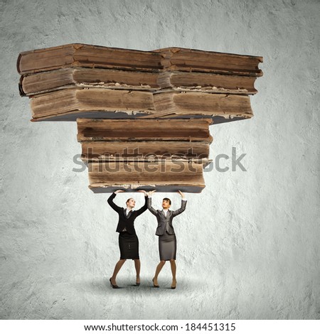 Two young ladies lifting pile of old books above head