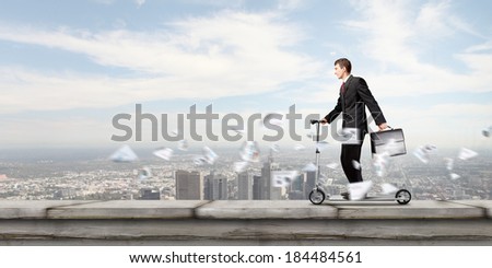Young businessman riding scooter on roof of building