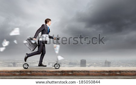 Young cheerful businessman riding scooter against city background