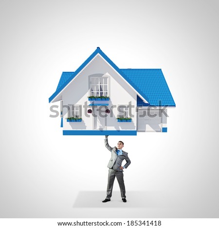 Young businessman lifting huge model of house above head Young businessman lifting huge model of house above head