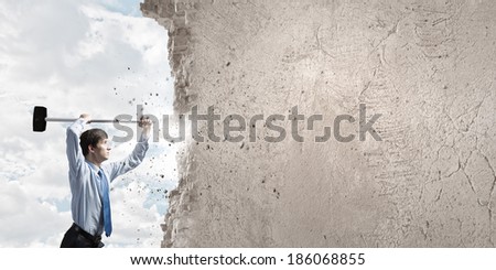 Young determined businessman breaking wall with hammer