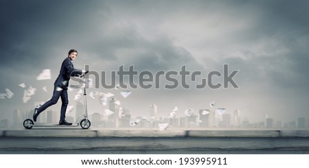 Young cheerful businessman riding scooter against city background