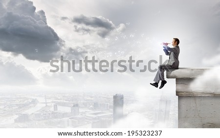 Young carefree businessman sitting on top of building and playing flute