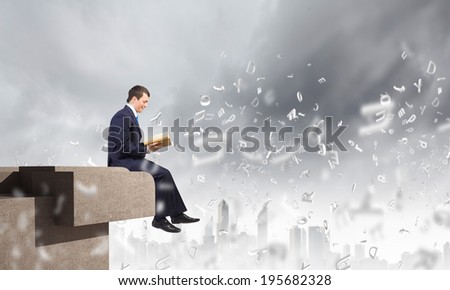 Young businessman sitting on top of building and reading book